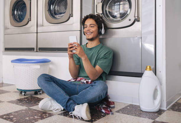mec utilisant smartphone laver des vêtements dans la machine au service de blanchisserie - all laundry detergent audio photos et images de collection