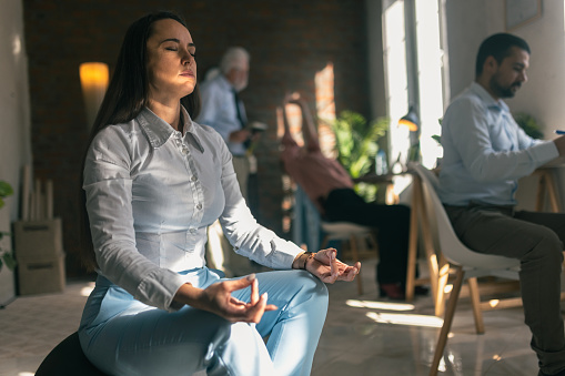 Shot of a young businesswoman meditating in a modern office while sitting on the fitnessball