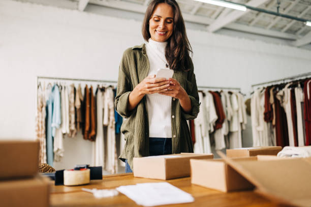 istock Female entrepreneur using a mobile phone as she processes clothing orders for shipping 1772382031