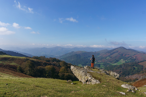 Hiking man standing on rock in beautiful basque countryside with meadow on the hill at the spanish french border near Beartzun, Navarre, Spain