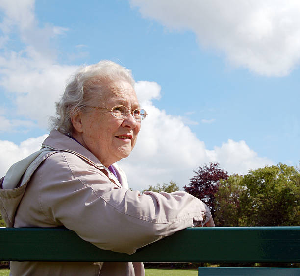 Senior lady sitting on a park bench stock photo