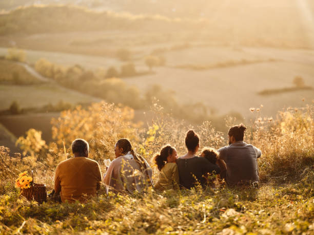 Back view of black multi-generation family relaxing in grass on a hill.