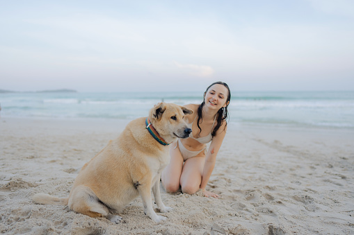 Woman resting with dog on the beach and sunbathing during vacation