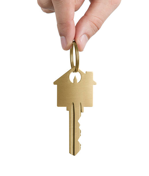 Hand holding gold house shaped key Human hand holding key to a dream house isolated on white background house key stock pictures, royalty-free photos & images