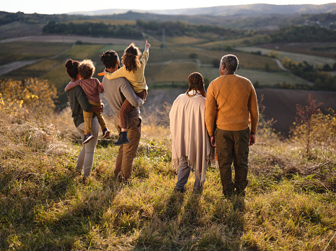 Rear view of African American extended family looking at view during autumn day from a hill. Girl is aiming at distance.