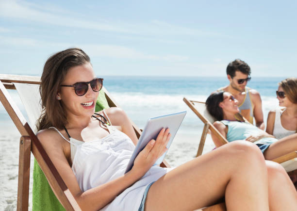 femme heureuse à l'aide de tablette numérique dans une chaise longue sur la plage - reading beach e reader men photos et images de collection