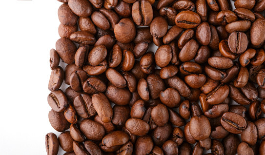 Cup of coffee with roasted coffee beans against a white background, high angle view.
