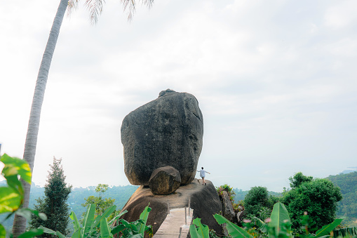 Young woman in white shirt  near the rock stuck on the mountain overlooking Ko Samui island