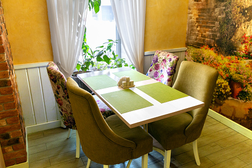 Interior of cozy living room in restaurant - table for four guests by the window with fresh flowers