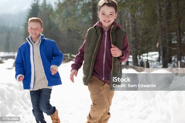 Portrait Of Happy Boys Running In Snowy Lane Stock Photo - Download Image Now - Front View, Running, Boys