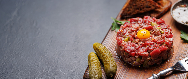 Savory beef tartare with pickled gherkins and brown bread toasts. With copy space