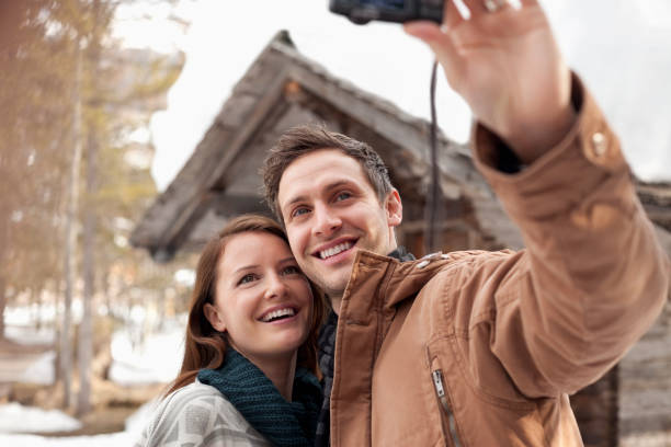 istock Smiling couple taking self-portrait with digital camera outside snowy cabin 177242826