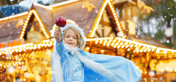 Little girl as snow white with candy sweet caramel apple from a sweets stand on Christmas market.