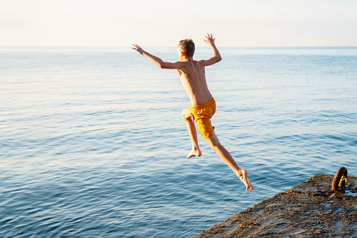 Teenagers having fun jumping from a cliff in to the sea