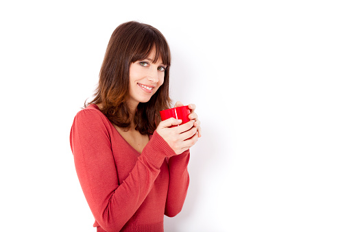 Beautiful young woman holding a cup of coffee, against a white wall