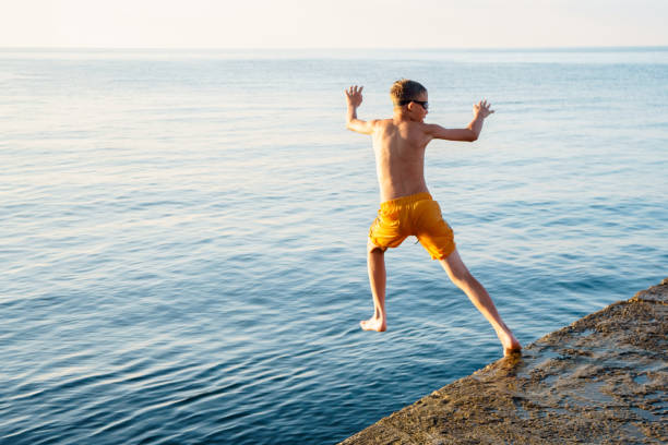 istock Healthy boy jumps into tranquil ocean water from stone pier 1772439226