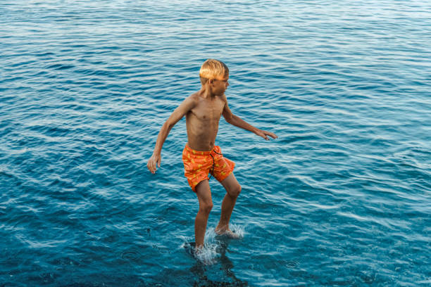istock Boy jumps from stone pier to sea touching water 1772440909