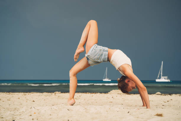 Yoga on the beach. Woman practicing yoga on coastline of the ocean. Beautiful girl relaxing by the sea. Calm, serene, minimalist photo with copy space. Healthy active lifestyle, vitality, zen.