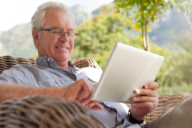 smiling senior man using digital tablet on patio - 銀髮族網民 個照片及圖片檔