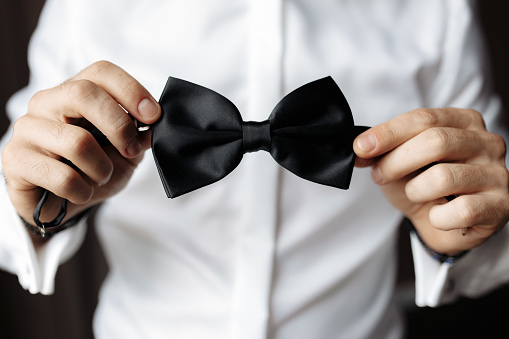 Partial close up view of man holding black bow tie. Soft focus high quality image.