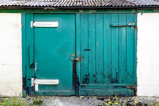 Pair mis-matched padlocked but delapidated and rotten wooden green garage doors with flaking and peeling paint Helensburgh, Argyll & Bute, Scotland, UK –07-27-2023.