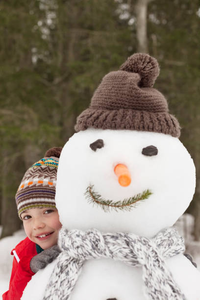 Smiling beautiful little girl hugging white snowman at nature park. Cute 4 years old toddler enjoying cold winter day. Front view. Posing and looking at camera.