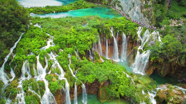 Crowd of tourists visit famous Plitvice waterfalls in Croatia. Mountain streams flow into a lake with azure clear water.