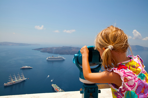 A girl uses binoculars above the sea in Santorini Greece
