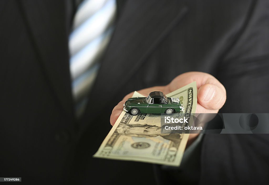 Sales agent offering a car "Sales agent offering car, holding a toy car and a dollar bill" Business Stock Photo