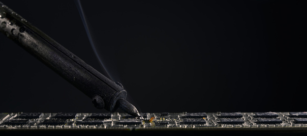 Horizontal shot of repair of the chip. An old soldering iron is soldering a microchip in close-up. Technician engineer in workshop.