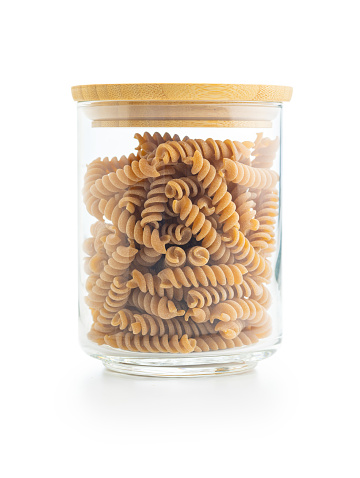Raw whole grain fusilli pasta. Uncooked pasta in jar isolated on the white background.
