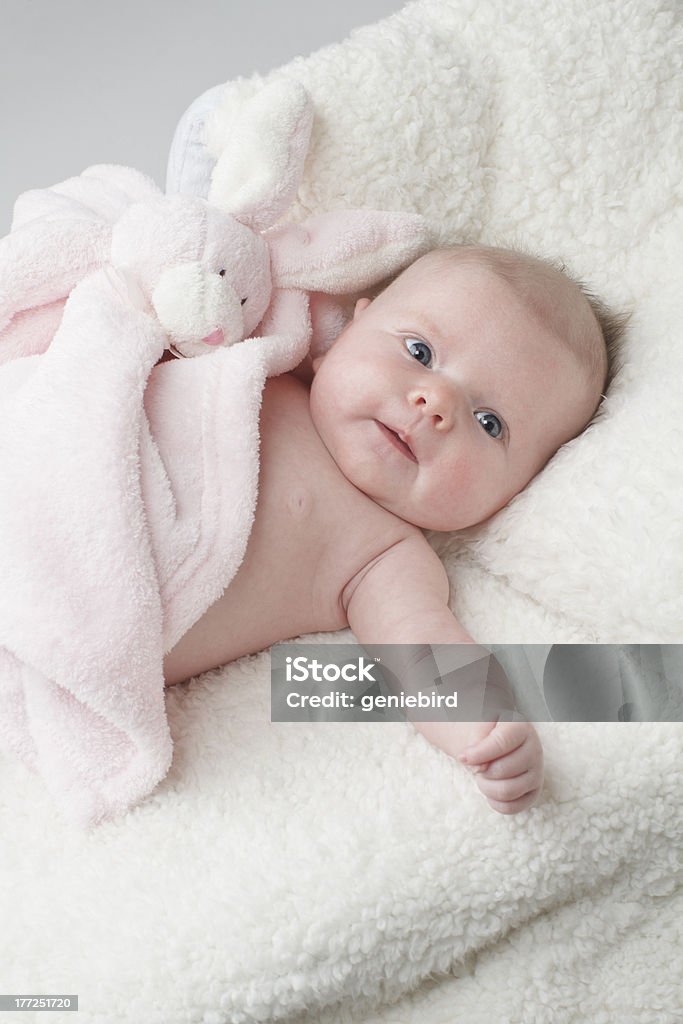 Happy baby with pink toy bunny blanket "Happy baby lying on white furry blanket with pink toy rabbit, vertical layout with copy space." Animal Stock Photo