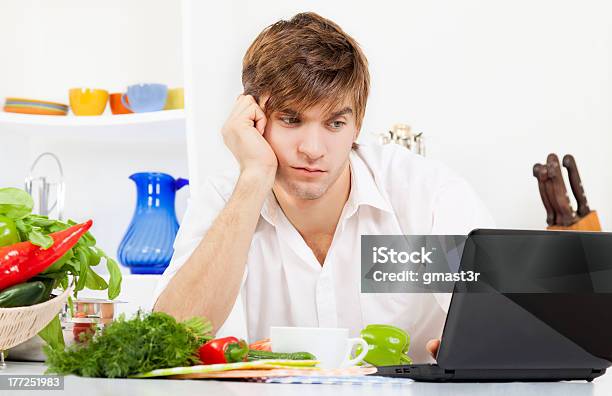 Young Man Looking Up Recipes On The Laptop In The Kitchen Stock Photo - Download Image Now