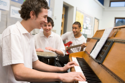 Schoolboys playing musical instruments in music class laughing together