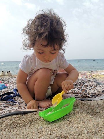 A closeup of a  child playing with toys on the sun-soaked beach, with the ocean in the background