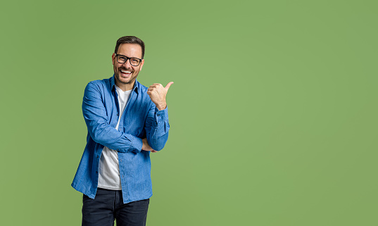 Cheerful young businessman aiming at copy space for marketing while standing on green background