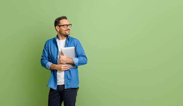 istock Young smiling businessman holding digital tablet and thinking while looking away on green background 1772538735