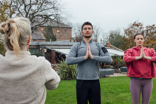 A young couple on a staycation together at Newton Hall in Northumberland, North East England. They are taking part in a yoga class outdoors and doing the mountain with prayer hands pose while standing side by side and following the yoga instructor at the front of the class.

Videos also available for this scenario.