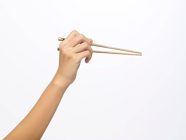 Hand holding golden chopsticks Female hand holding a pair of golden chopsticks, isolated on white background. right handed stock pictures, royalty-free photos & images