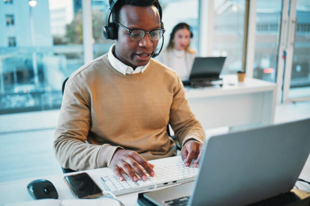 istock Business man, call center and typing on computer for communication, customer support and advice in workspace. Professional agent, African consultant or web advisor for contact, FAQ and help on laptop 1772589411