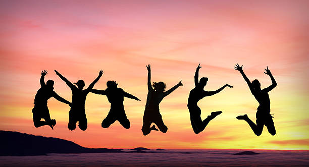 silhouette of female friends jumping in sunset stock photo