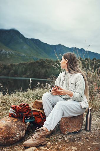 Camping, phone and woman relax in nature with social media, freedom or outdoor peace. Hiking, break and female explorer with smartphone, app or chat while chilling at forest lake and enjoying scenery