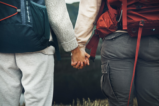 Couple, holding hands and backpack in nature for hiking, adventure or outdoor journey together. Rear view or closeup of hiker, people or backpacking in teamwork for trekking, motivation or support