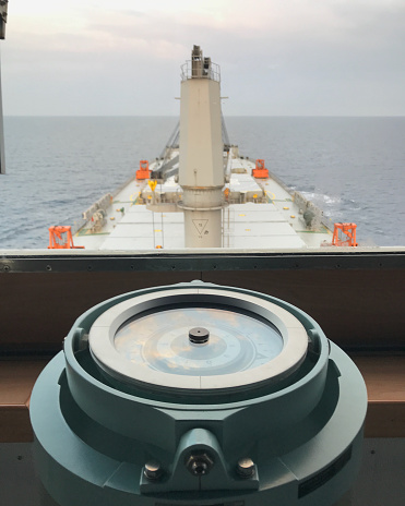 Merchant ship carrying bulk cargo is underway at sea and gyro compass in the foreground