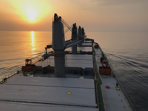 Merchant ship carrying bulk cargo is underway at sea in the evening during sunset