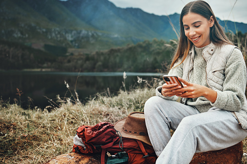 Nature, smile and woman on a phone for hiking on a mountain and network on social media or mobile app. Happy, technology and young female person scroll on internet with cellphone in outdoor forest.