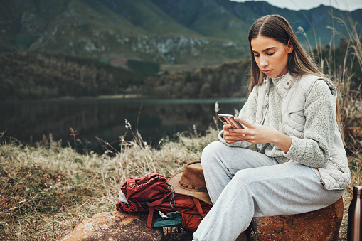 Nature, phone and young woman hiking on a mountain and network on social media or mobile app. Travel, technology and female person from Canada scroll on internet with cellphone in outdoor forest.