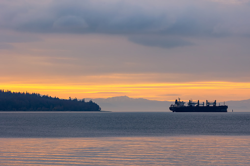 Vancouver, Canada - March 7, 2022 : Dramatic colorful sunset over freighter ships in English Bay and Burrard Inlet, seen from Stanley Park