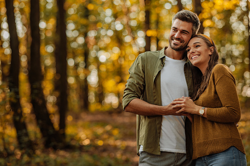 Beautiful, young, happy couple in love walking in the woods while holding hands and smiling, feeling in love