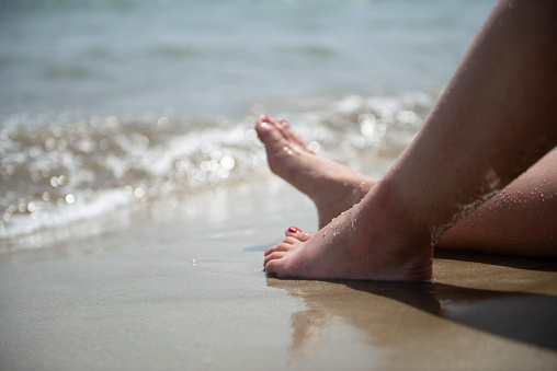 Sandy toes and feet of a couple on lounge chairs enjoying a beach vacation while watching their kids play in the sand. Tropical resort setting